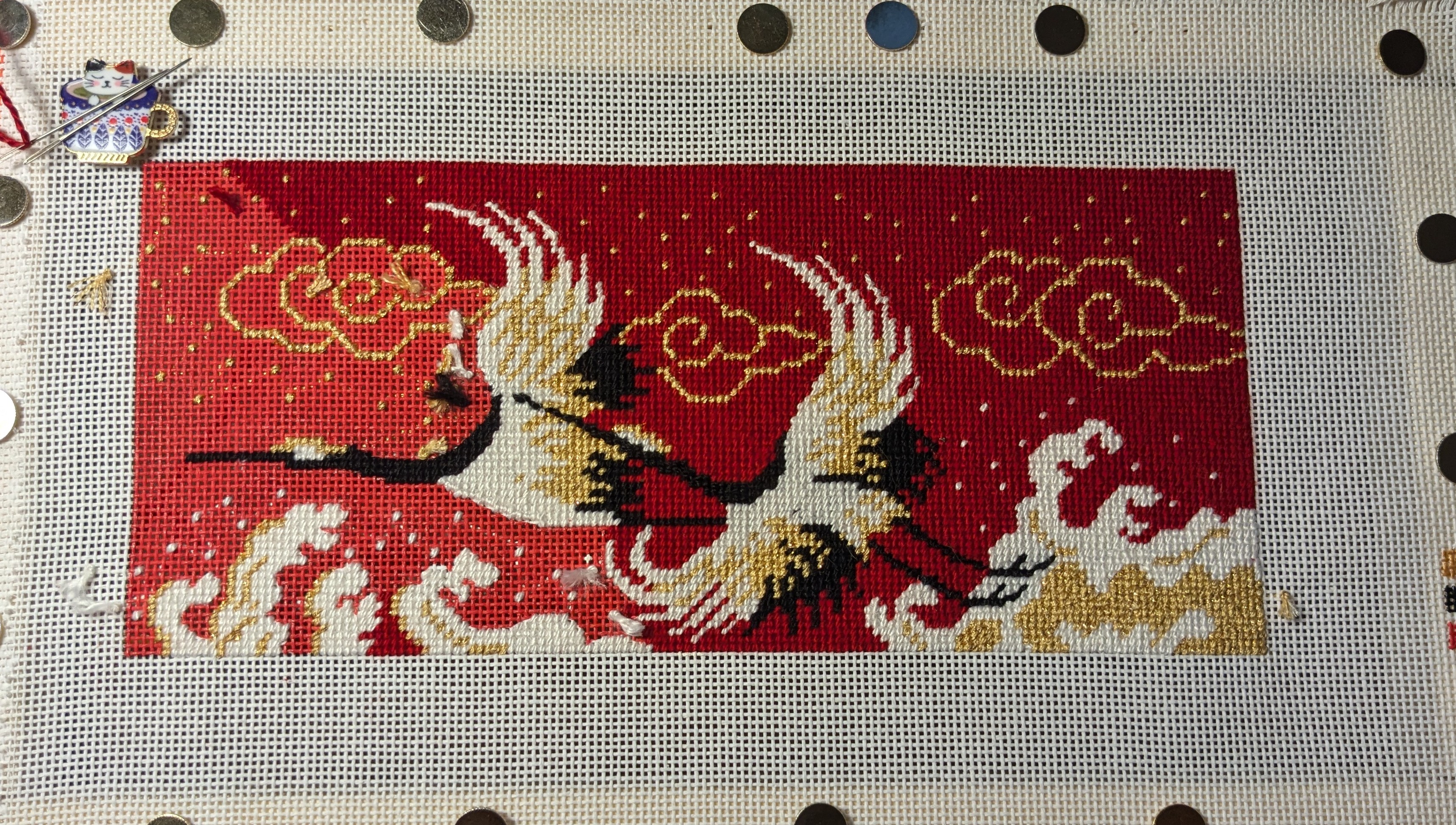 needlepoint: 2 storks flying across a red sky with white and gold clouds